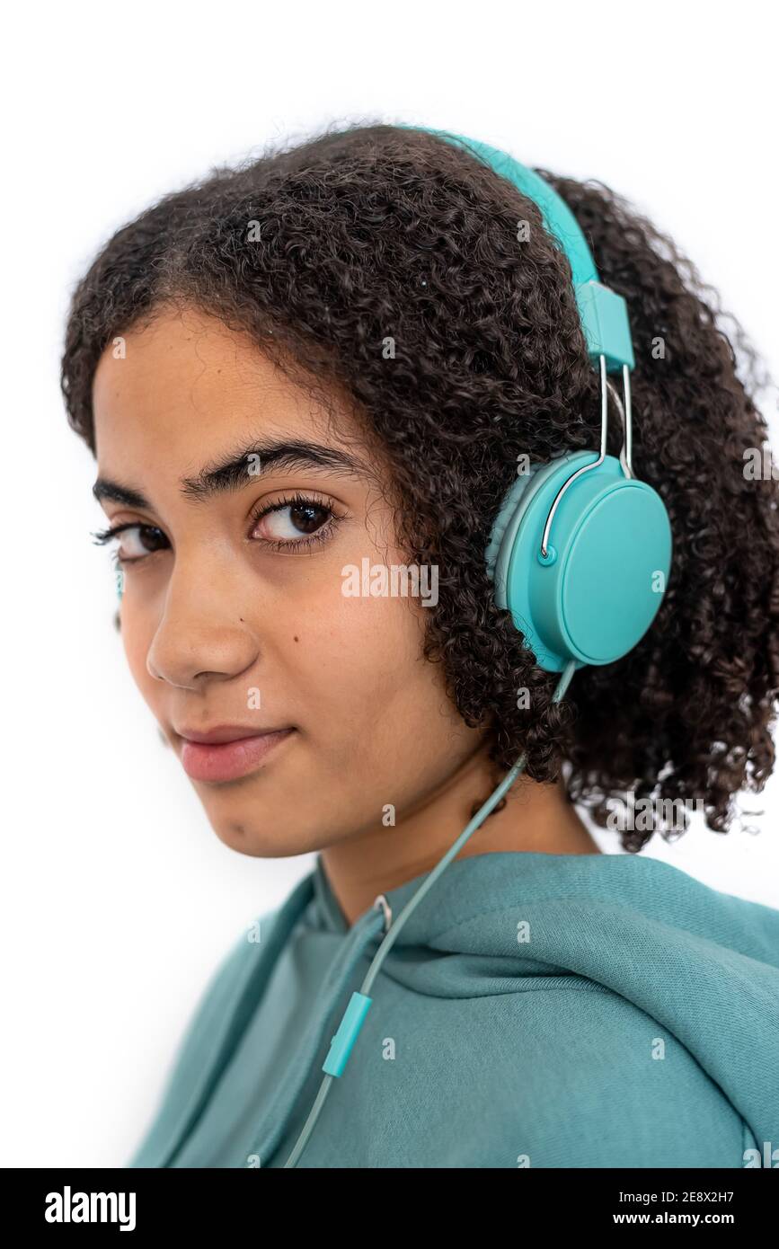 Teenager afroamericano con capelli ricci guardando la macchina fotografica e. ascolto di musica con le moderne cuffie turchesi Foto Stock