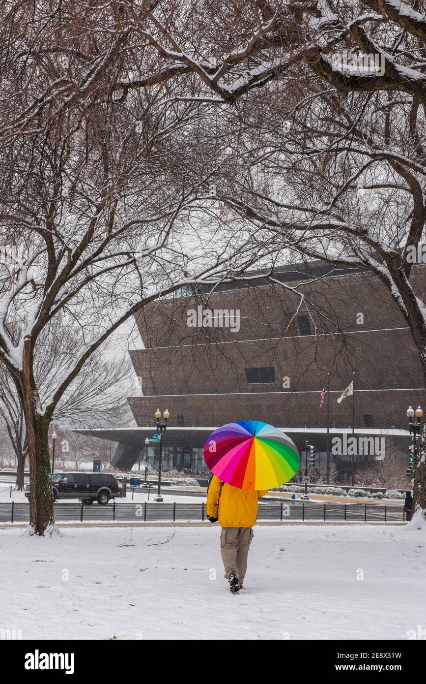 Un uomo con un ombrello colorato cammina oltre lo Smithsonian National Museum of African American History and Culture (NMAAHC) durante Una giornata innevata a Washi Foto Stock