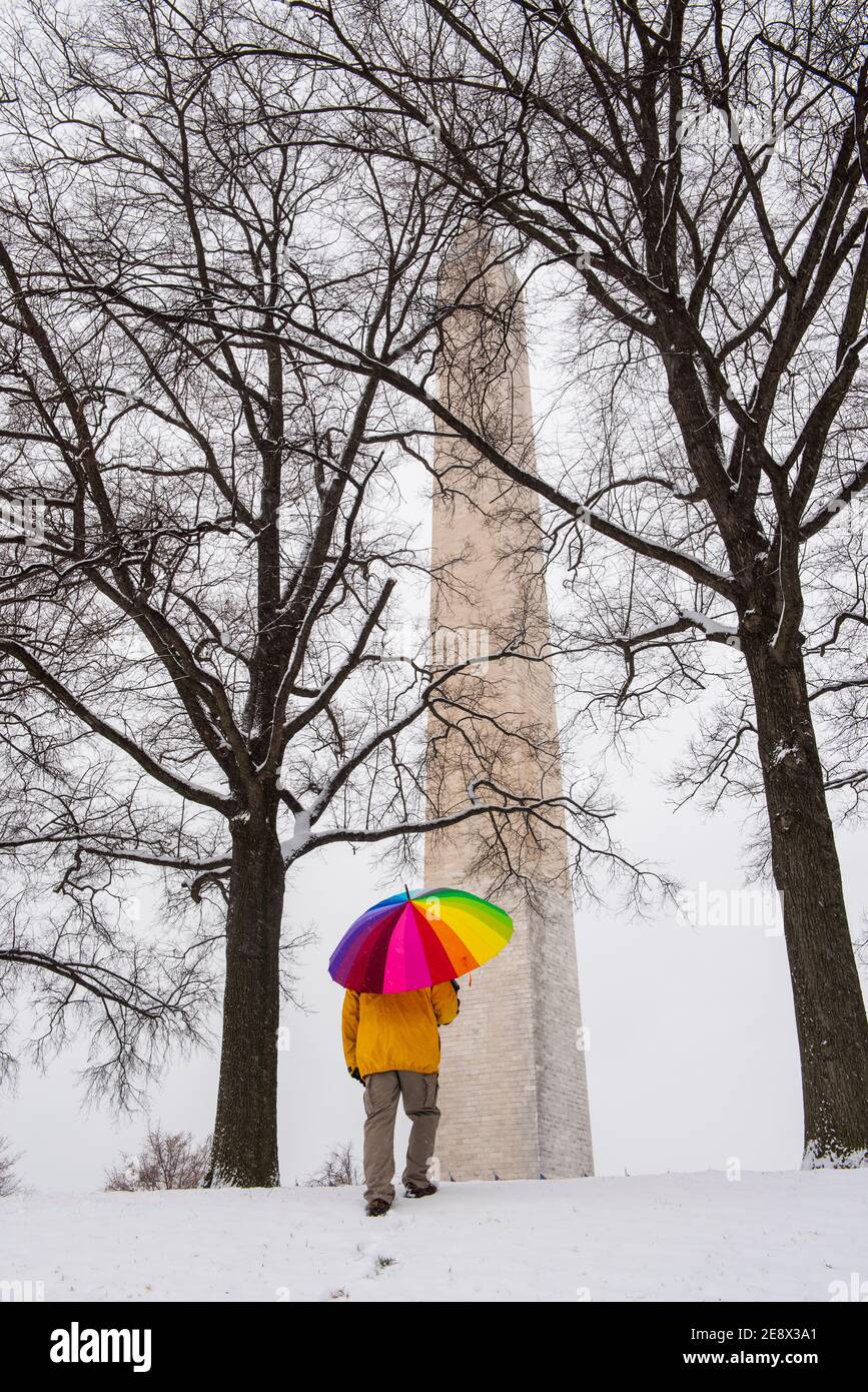 Un uomo che porta un ombrello colorato cammina verso il monumento di Washignton durante una giornata di neve sul National Mall di Washington, D.C. Foto Stock