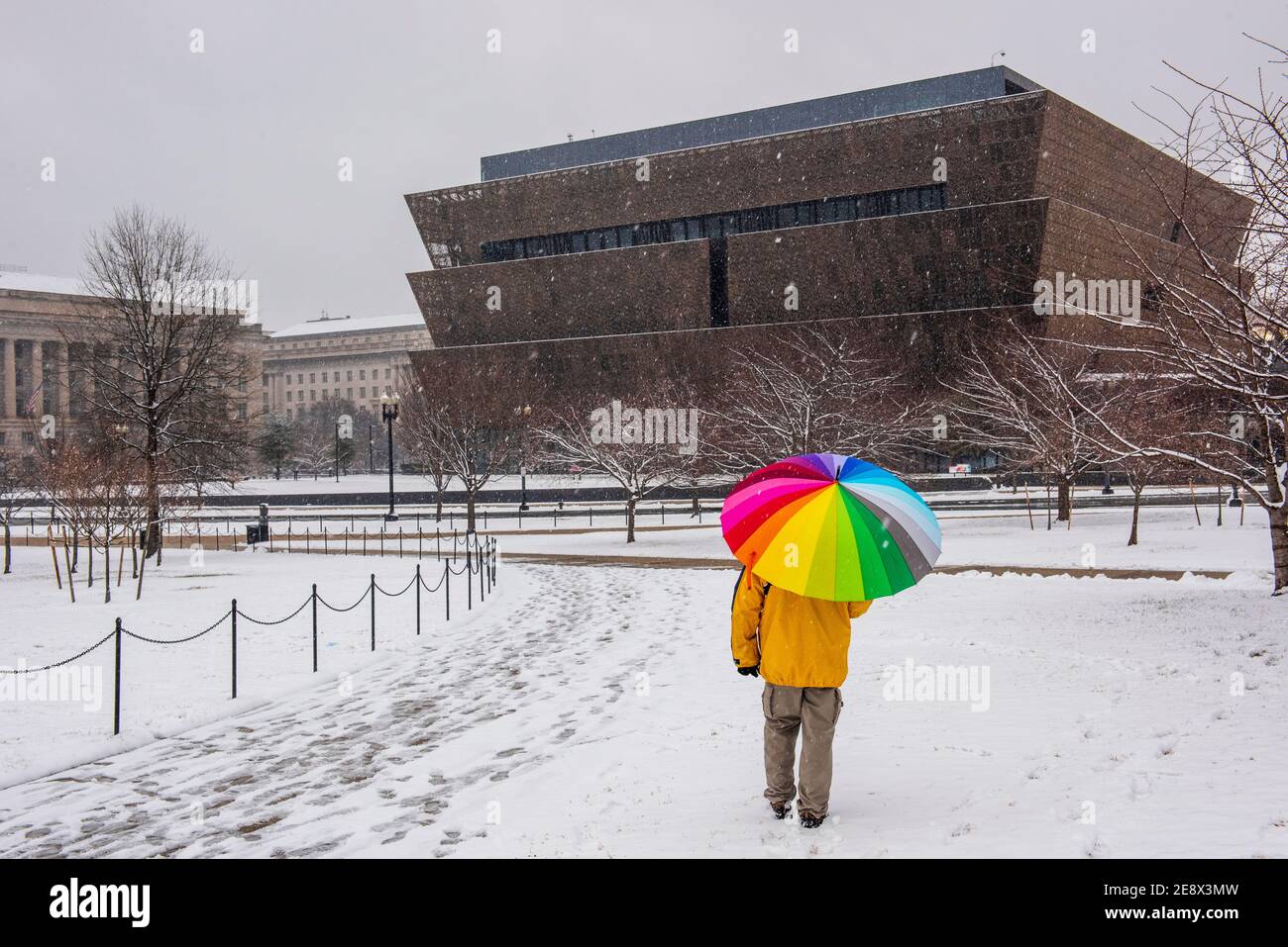 Un uomo con un ombrello colorato cammina oltre lo Smithsonian National Museum of African American History and Culture (NMAAHC) durante Una giornata innevata a Washi Foto Stock