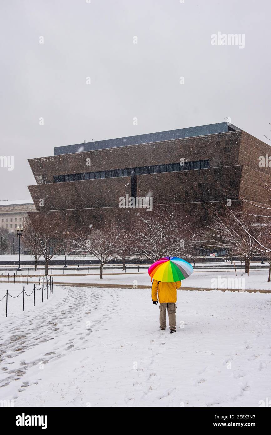 Un uomo con un ombrello colorato cammina oltre lo Smithsonian National Museum of African American History and Culture (NMAAHC) durante Una giornata innevata a Washi Foto Stock