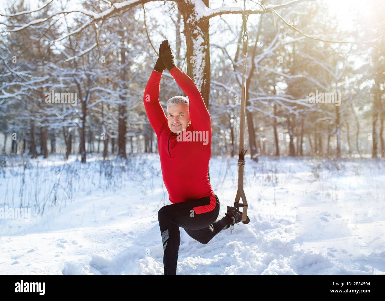 Concetto di fitness invernale all'aperto. Allenamenti sportivi con cinghie TRX Resistance nella foresta innevata Foto Stock