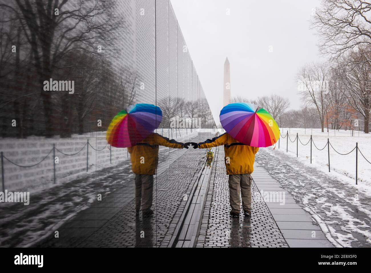 Un uomo che porta un ombrello colorato visita il Vietnam Veterans Memorial durante una giornata innevata a Washington, D.C. il Washington Monument può essere visto in th Foto Stock