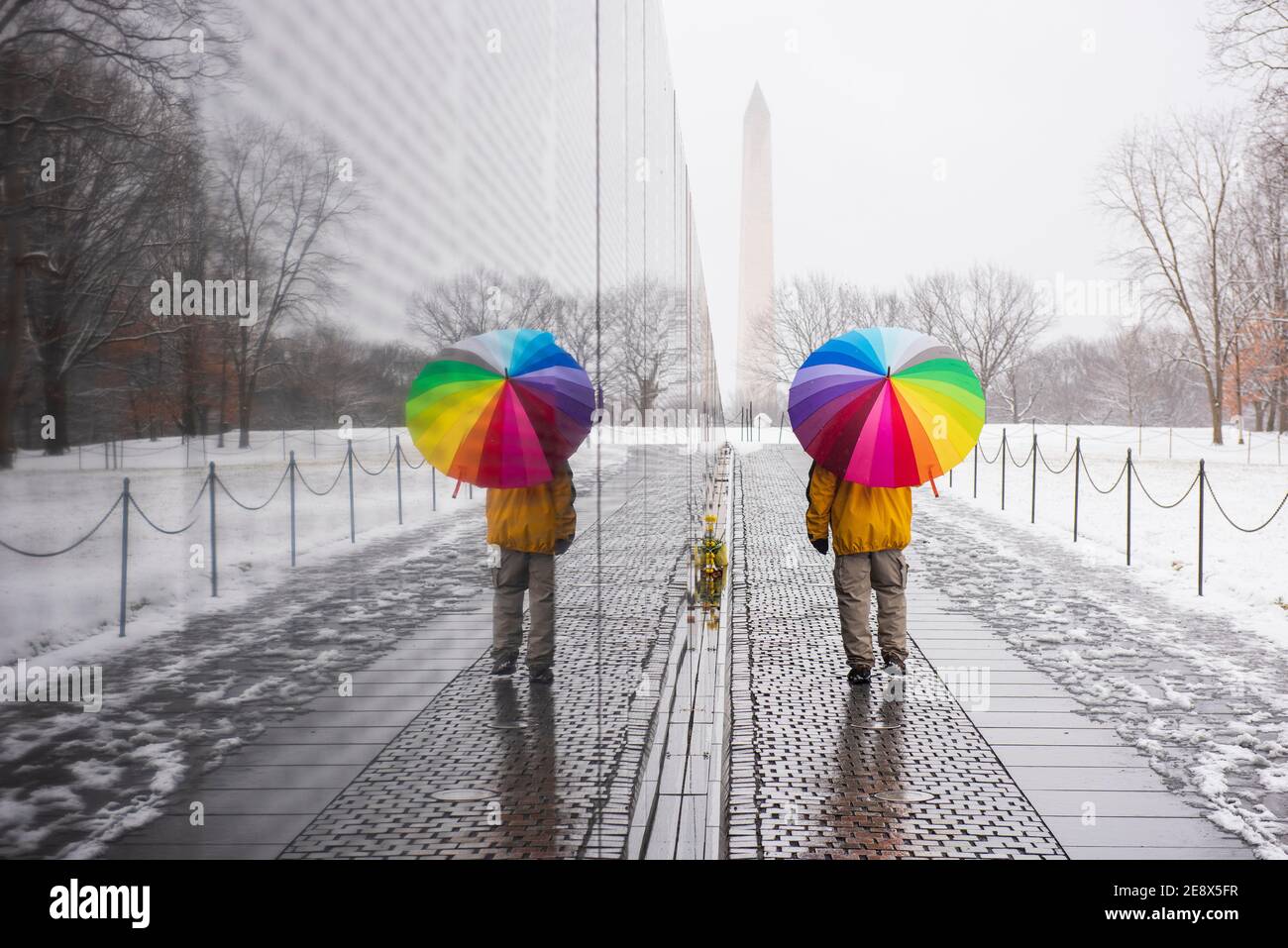 Un uomo che porta un ombrello colorato visita il Vietnam Veterans Memorial durante una giornata innevata a Washington, D.C. il Washington Monument può essere visto in th Foto Stock