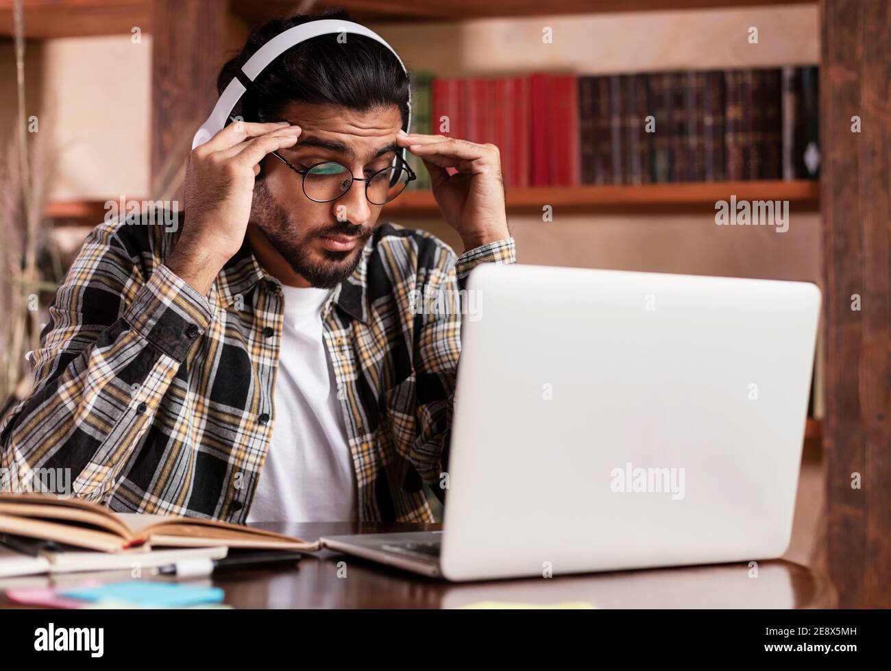 Studente stanco seduto al portatile e Libri imparare in biblioteca Foto Stock