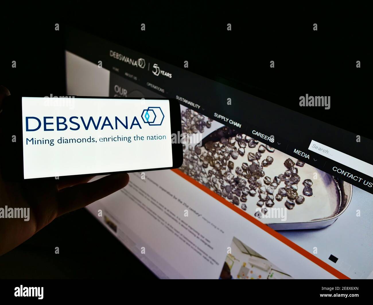Persona che tiene il cellulare con il logo della società mineraria Debswana Diamond Company Limited in esposizione davanti al sito web aziendale. Mettere a fuoco lo schermo del telefono. Foto Stock
