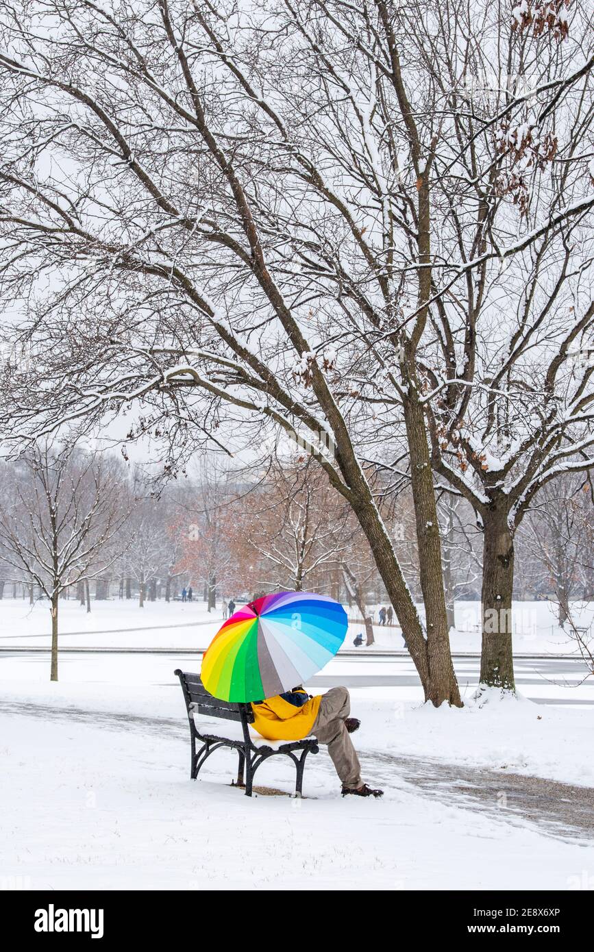 Un uomo che porta un ombrello colorato visita Constitution Gardens durante una giornata innevata a Washington, D.C. Foto Stock