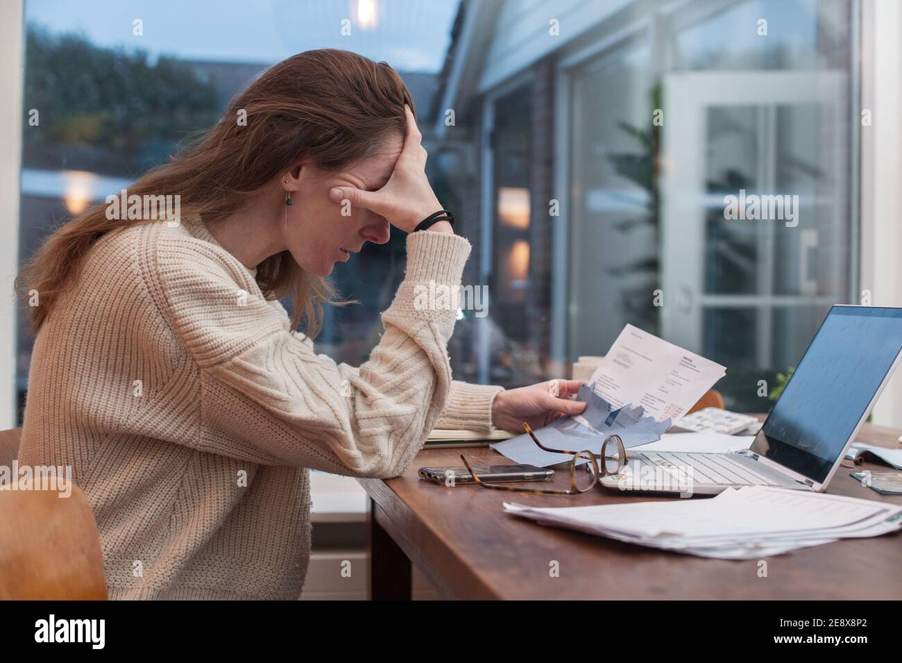 Una giovane donna con preoccupazioni finanziarie in un ambiente domestico sentirsi triste e sottolineato dalla sua situazione finanziaria Foto Stock