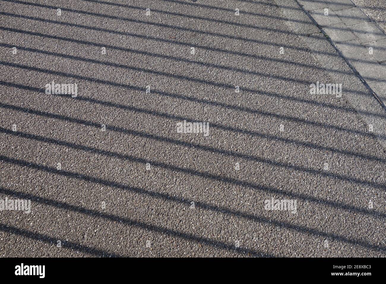 L'ombra di una recinzione su una passeggiata pedonale. Sfondo grigio creato su asfalto. Foto Stock