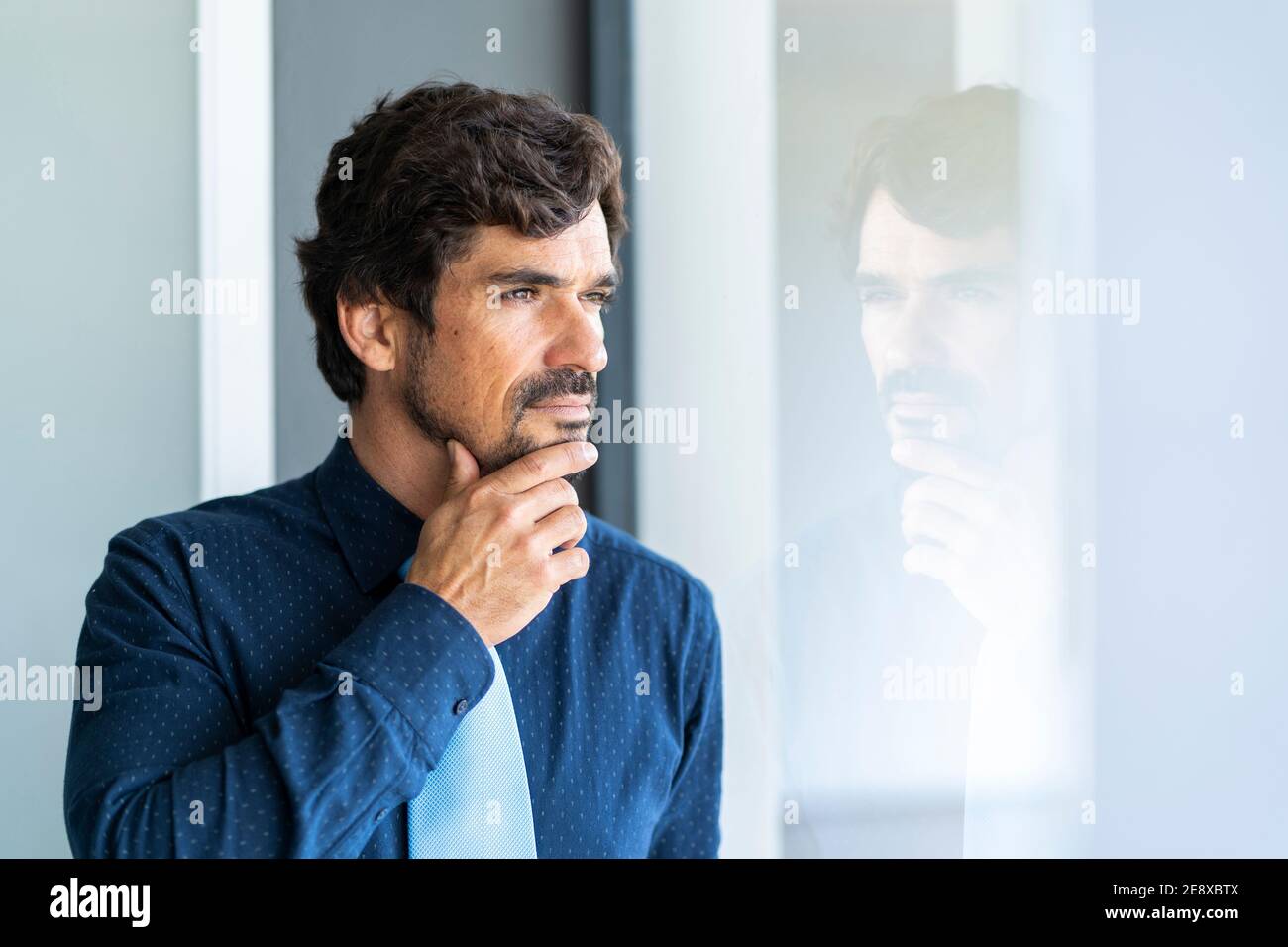 Uomo d'affari che guarda attraverso la finestra. Ritratto maschile di successo in ufficio con la giusta attenzione, serietà e serena atteggiamento. Foto Stock