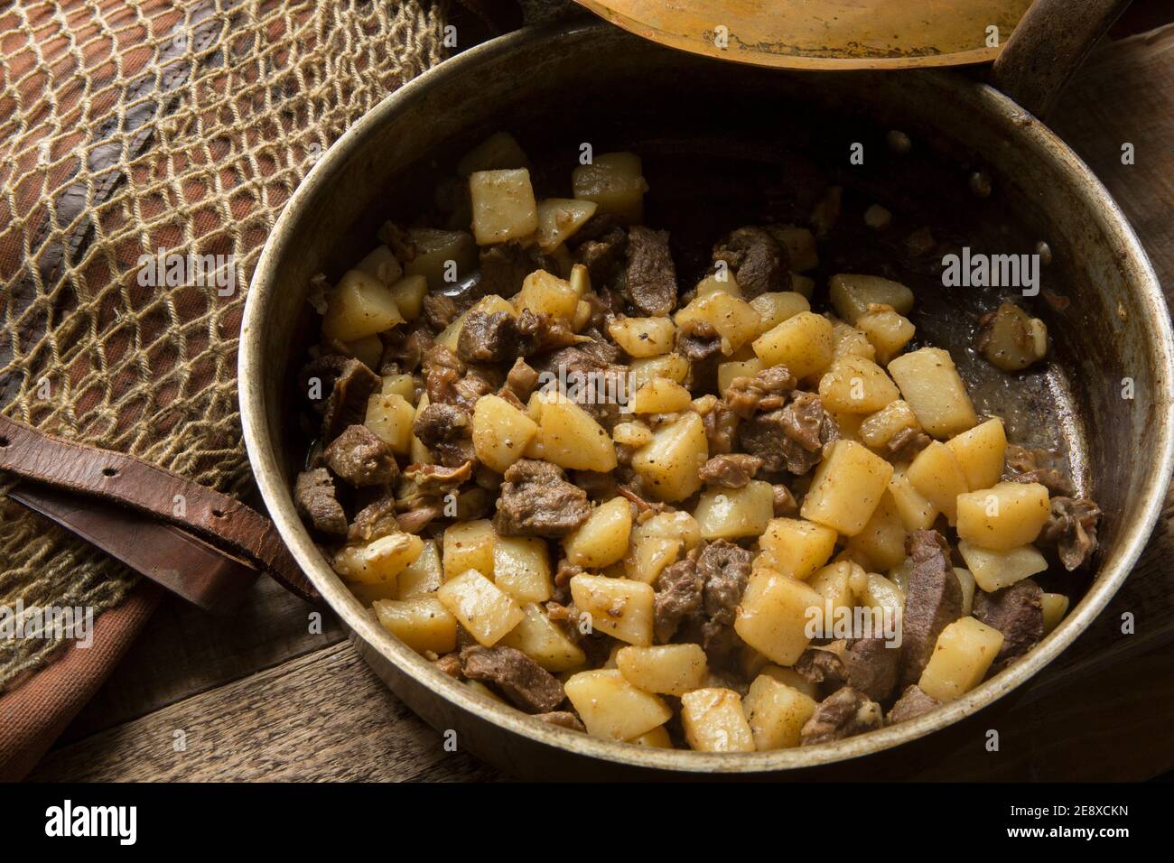 Pezzi di veleno di un cervo che è stato fritto con agnello a dadini e cotto con patate e aglio. Fatto in casa in una pentola di rame Foto Stock