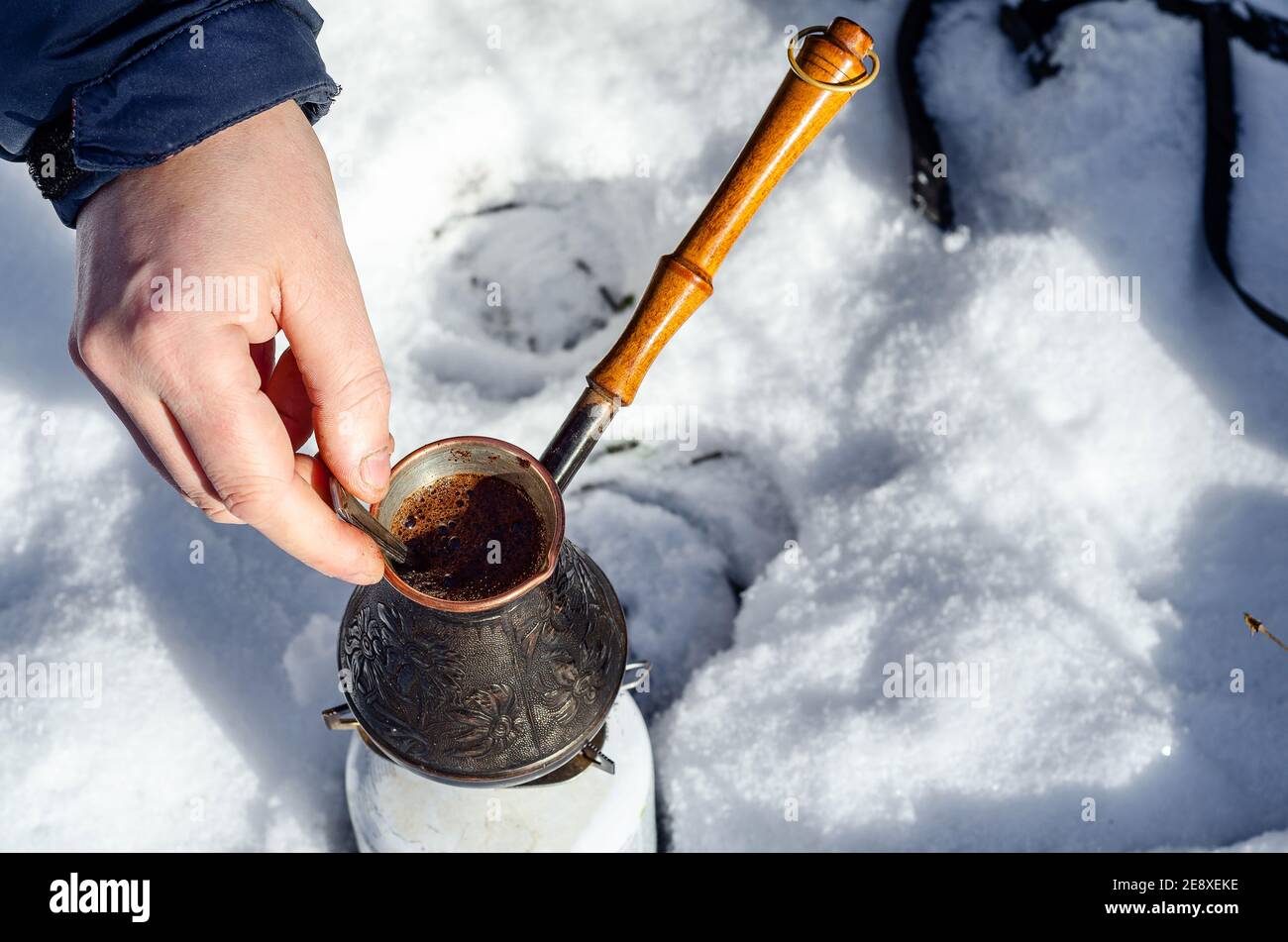 Cezve di rame, facendo il caffè nella natura, neve, foresta, mano dell'uomo miscela il caffè con il cucchiaio Foto Stock