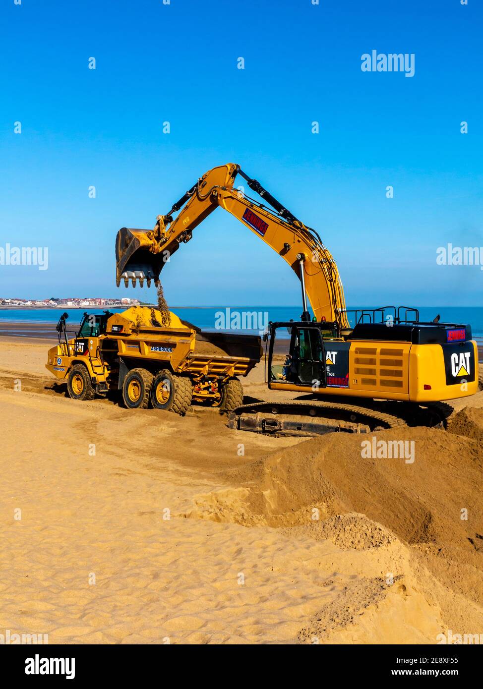 Digger meccanico e camion movimento terra che rimuove la sabbia dalla spiaggia a Colwyn Bay Conway Galles Regno Unito dopo gravi tempeste invernali ha spostato la sabbia. Foto Stock