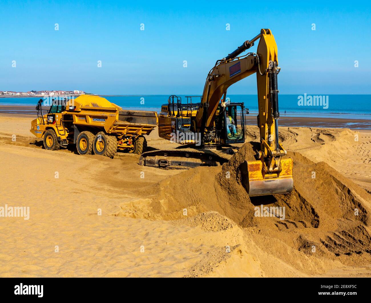 Digger meccanico e camion movimento terra che rimuove la sabbia dalla spiaggia a Colwyn Bay Conway Galles Regno Unito dopo gravi tempeste invernali ha spostato la sabbia. Foto Stock