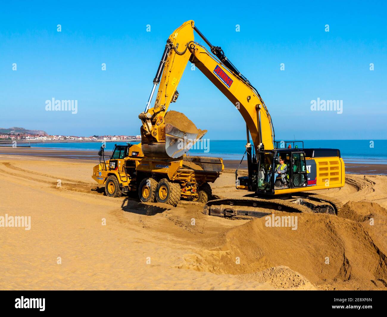 Digger meccanico e camion movimento terra che rimuove la sabbia dalla spiaggia a Colwyn Bay Conway Galles Regno Unito dopo gravi tempeste invernali ha spostato la sabbia. Foto Stock