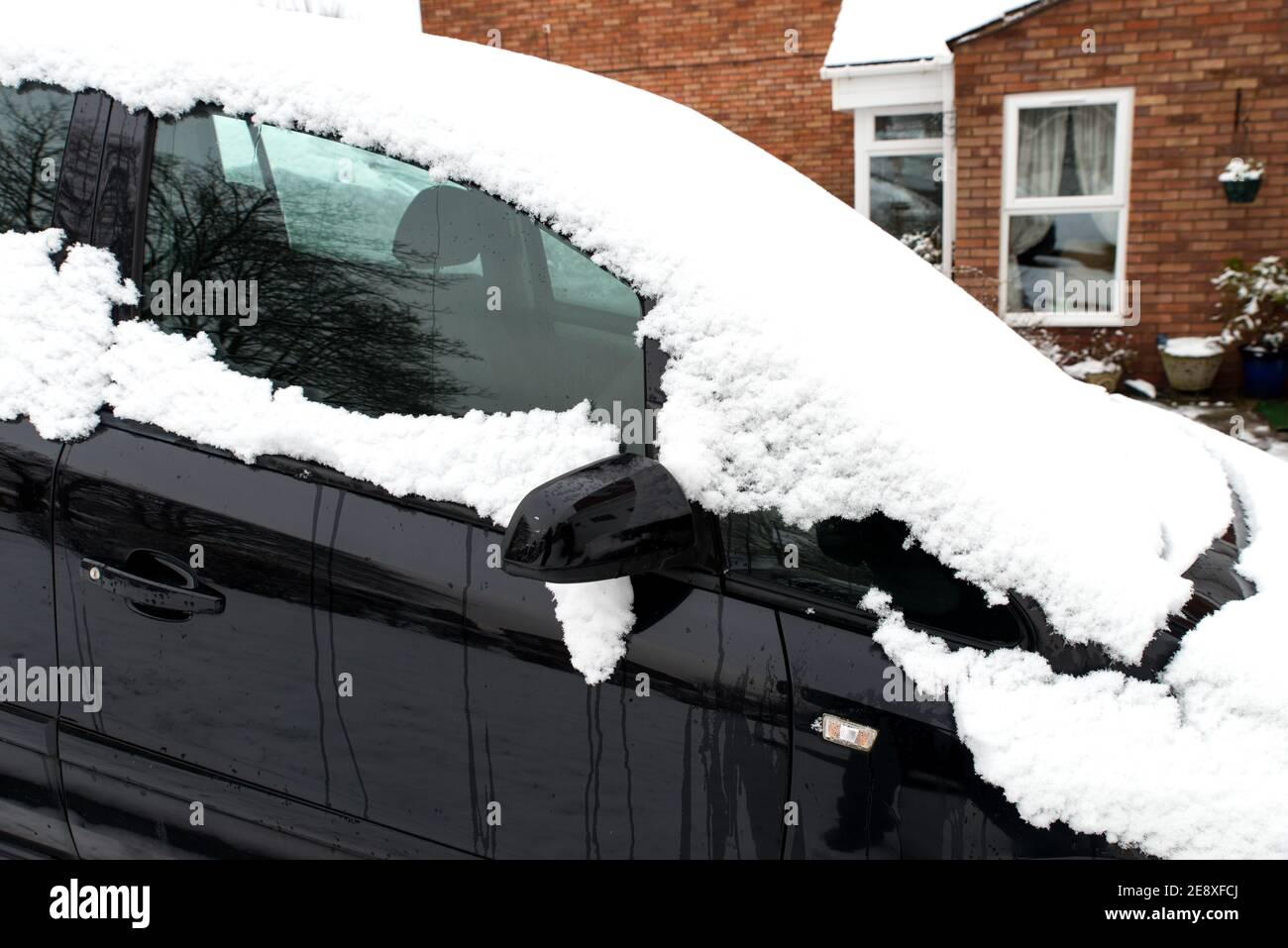 primo piano di auto nera coperta di neve. L'auto brillante è parcheggiata su un vialetto fuori casa domestica di mattoni in un giorno freddo degli inverni Foto Stock