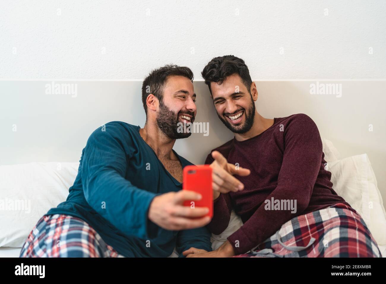 Felice coppia gay divertirsi utilizzando smartphone mobile a letto - amore omosessuale e concetto di tecnologia Foto Stock