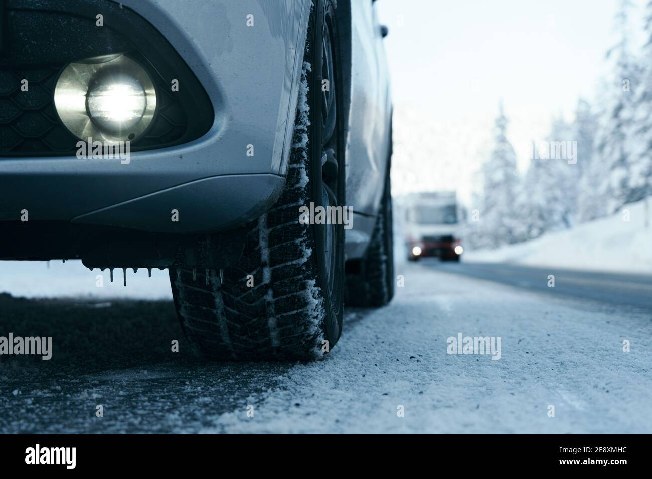 Primo piano di pneumatici invernali con ruota in lega e paraurti di veicolo sportivo di utilità su strada ghiacciata di montagna coperta di neve, Italia Foto Stock