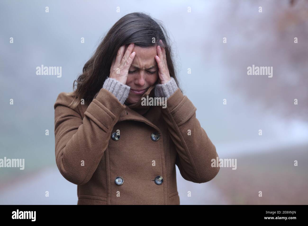 Donna triste in inverno lamentandosi di camminare da sola in un parco un giorno foggy Foto Stock
