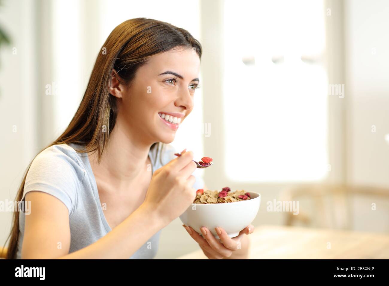 Donna felice che mangia cereali dal ciotola per la prima colazione nel soggiorno a casa Foto Stock