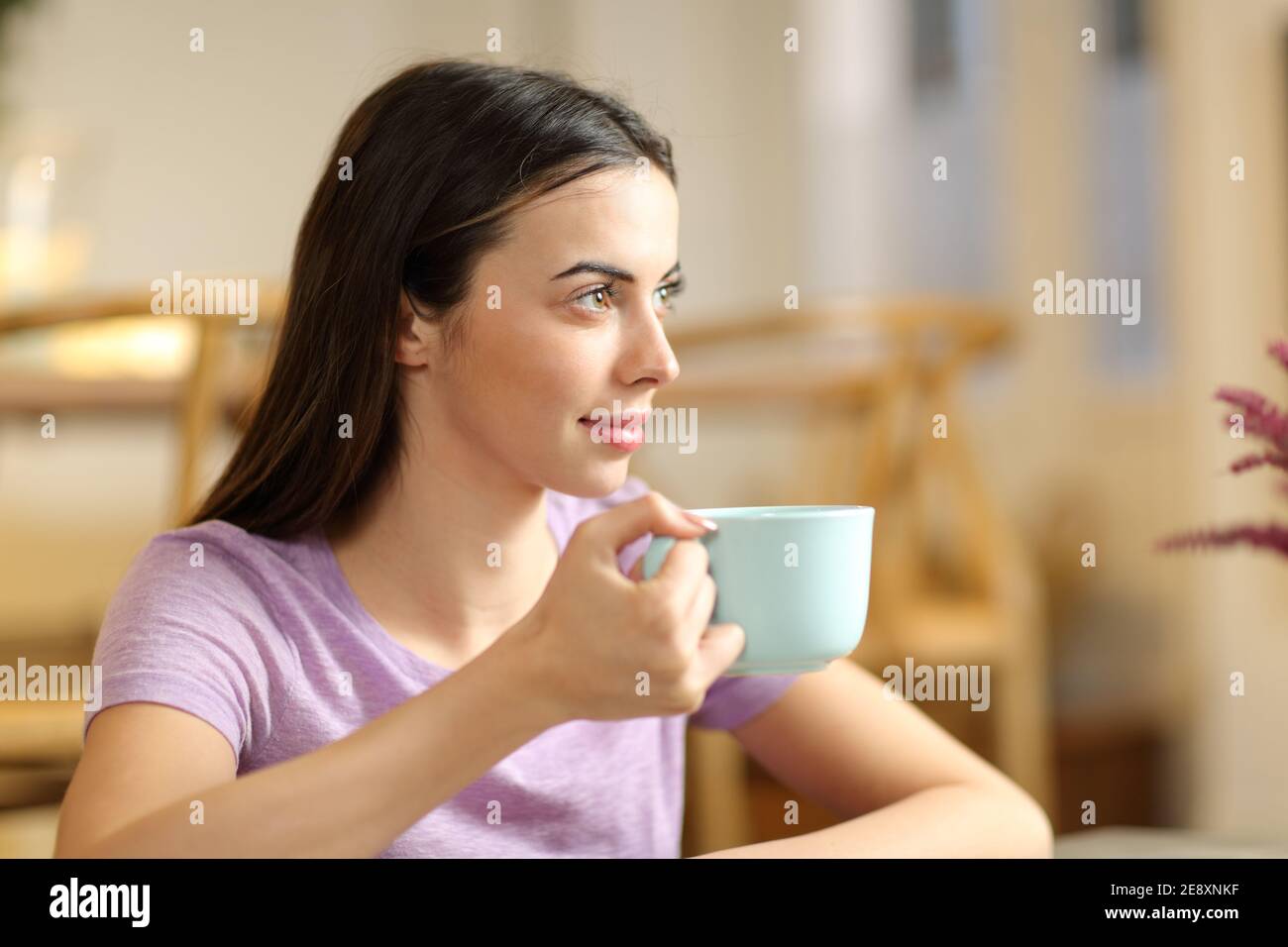 Donna rilassata che guarda via bere caffè seduto a casa Foto Stock