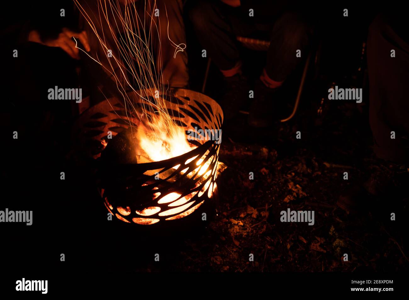 Fotografia a lunga esposizione di tre persone non identificate intorno ad un campo pit fuoco con un pezzo di legno su di esso il buio di notte con sfondo scuro Foto Stock