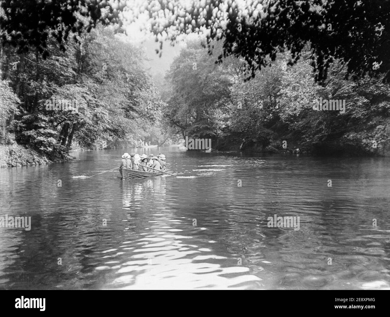 Una fotografia edoardiana in bianco e nero all'inizio del ventesimo secolo che mostra un gruppo di donne e ragazze in una barca a remi su un fiume in Inghilterra. Un uomo sta girovagando la barca. Foto Stock