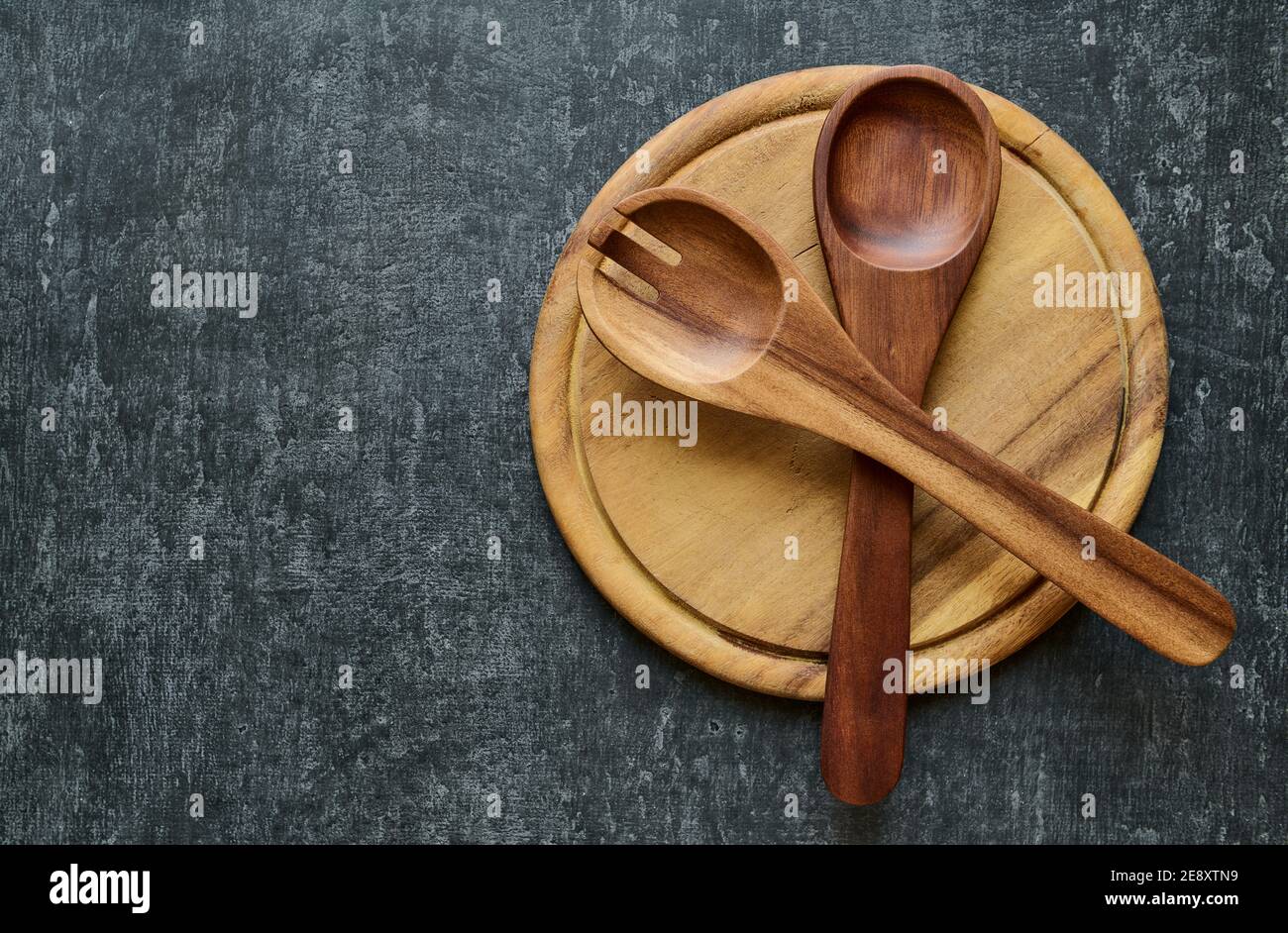 Utensili da cucina, cucchiai di insalata in legno si trovano trasversalmente su un tagliere rotondo, stile vintage. Vista dall'alto con luogo di copia Foto Stock