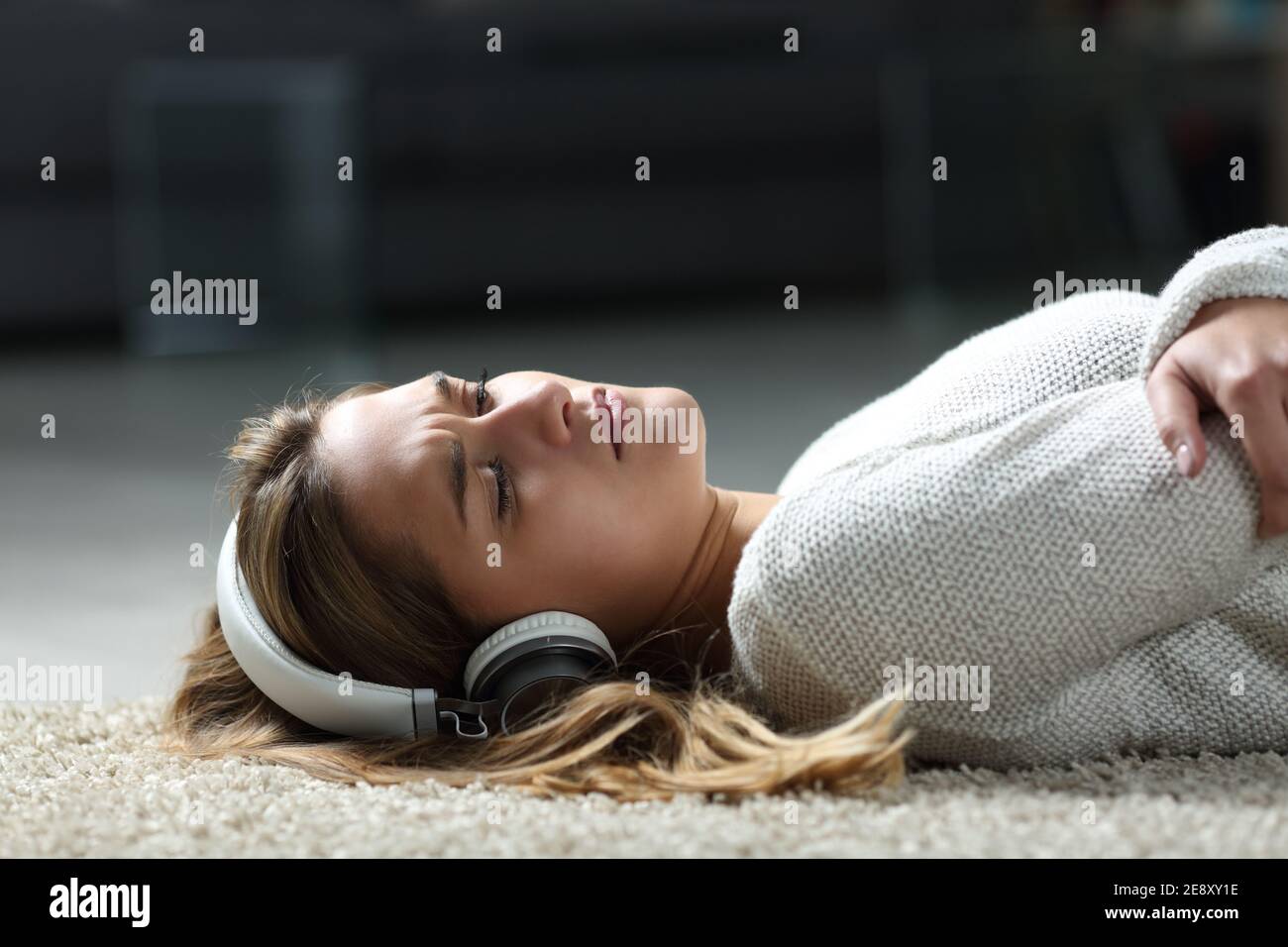 Donna triste che ascolta la musica indossando le cuffie sdraiate sul pavimento a casa Foto Stock