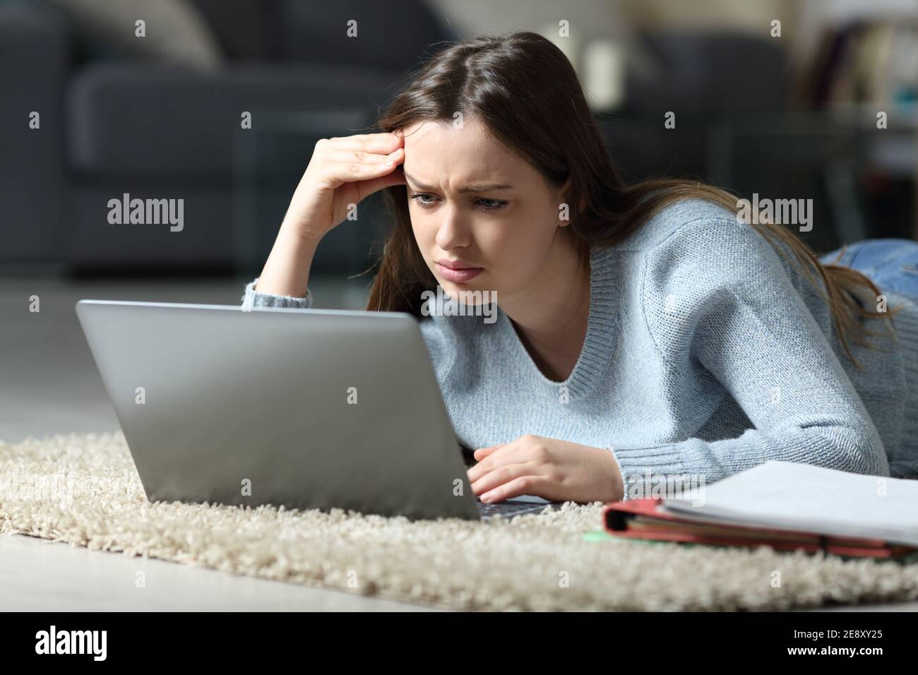E-learning degli studenti confuso utilizzando un computer portatile che si trova sul pavimento in casa Foto Stock