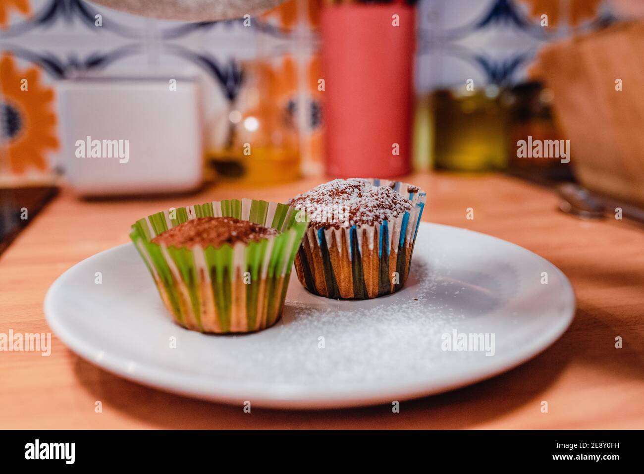 Muffin con zucchero a velo sulla parte superiore e involucri colorati un piatto sopra il bancone della cucina Foto Stock