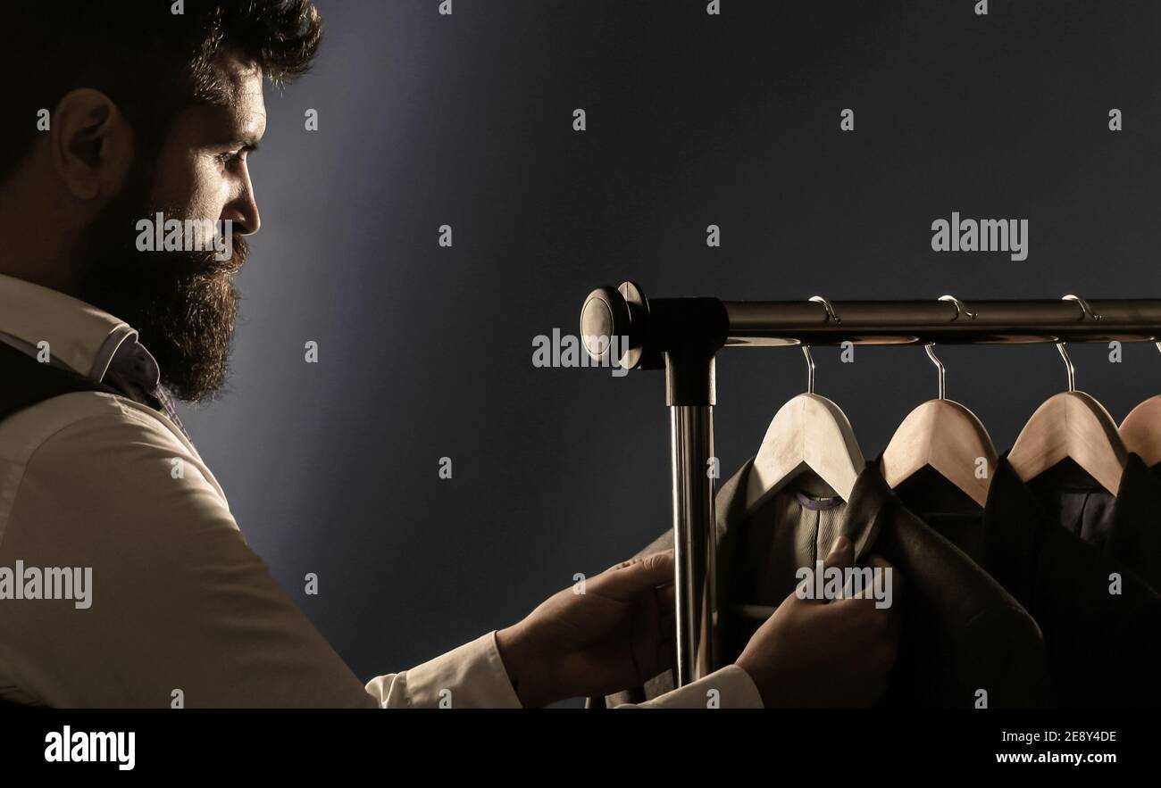 Su misura. Abito da uomo, sarto nella sua officina. Eleganti abiti da uomo appesi in fila. Abiti classici da uomo di lusso su rack in eleganti da uomo Foto Stock