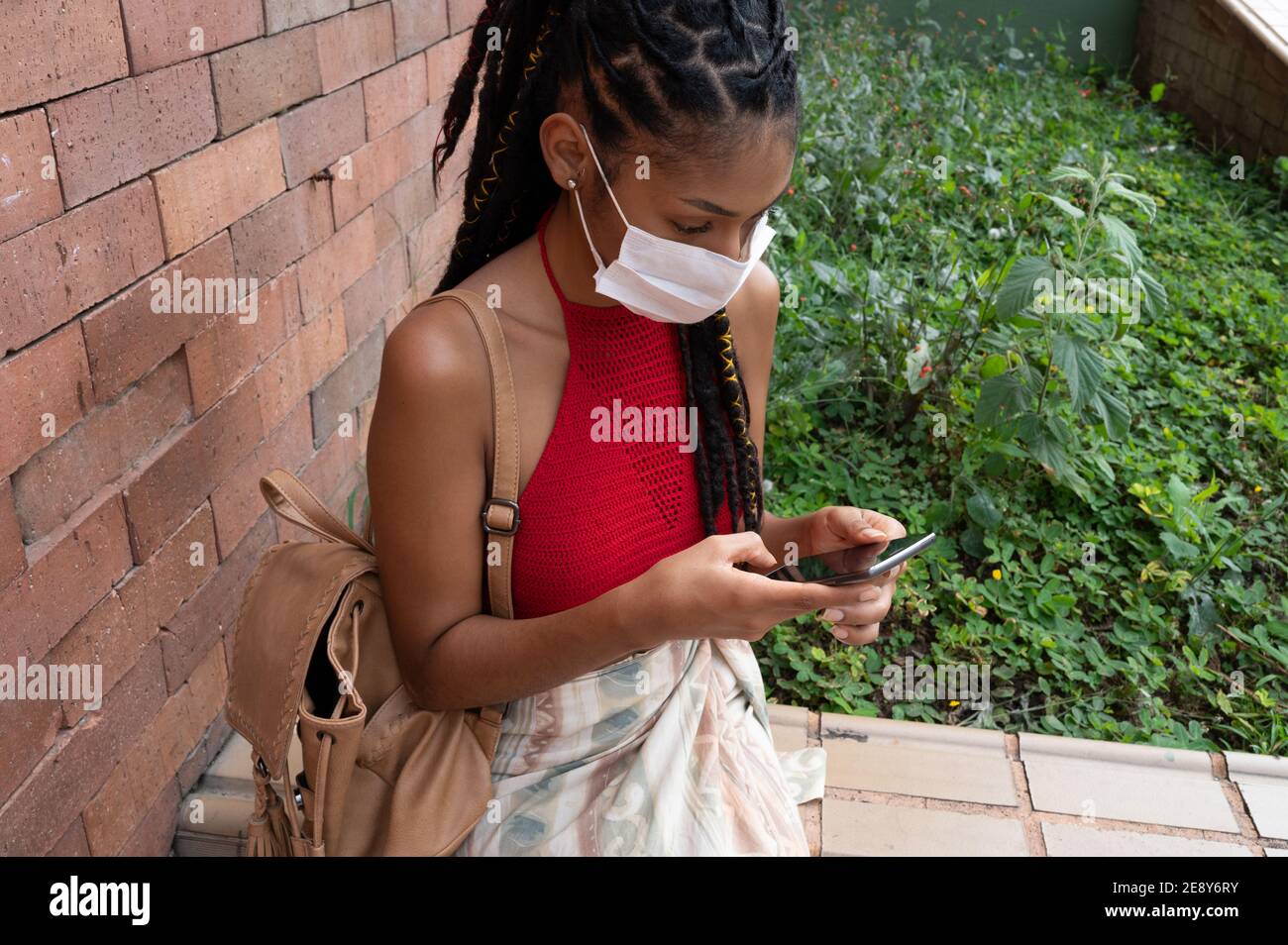 Giovane afrolatina donna in maschera con il suo smartphone in strada, Colombia Foto Stock