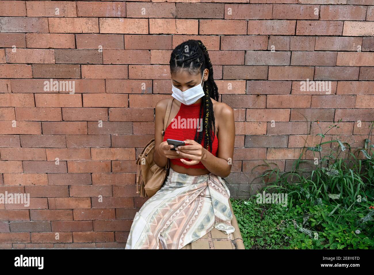 Giovane afrolatina donna in maschera con il suo smartphone in strada, Colombia Foto Stock