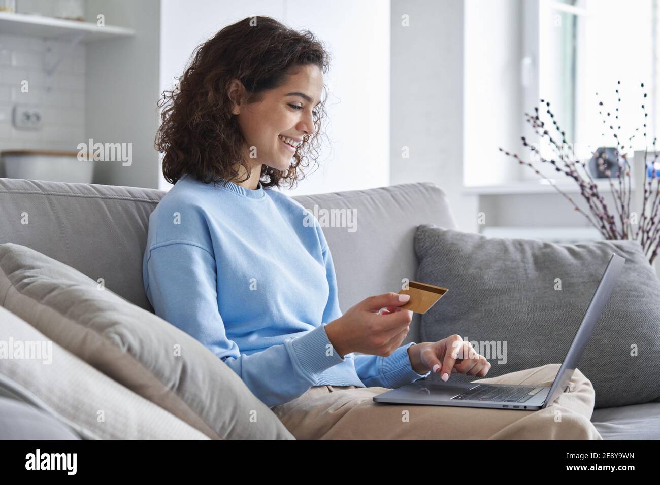 Felice giovane donna consumatore che tiene carta di credito e laptop che acquista online a casa. Foto Stock