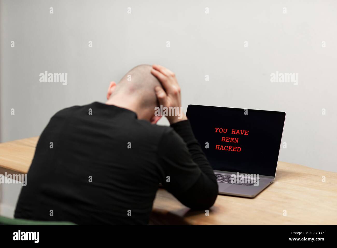 Testo rosso su un laptop che dice ‘sei stato violato’. Un uomo disperato seduto di fronte al suo computer infetto. Cybercrimine, infetto dispositivo non sicuro Foto Stock