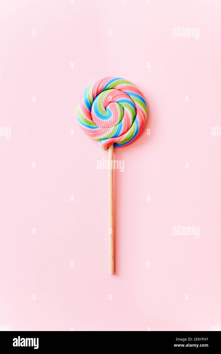 Coloratissima curva lollipop sul bastone. Caramelle multicolore a spirale su sfondo rosa, vista dall'alto Foto Stock