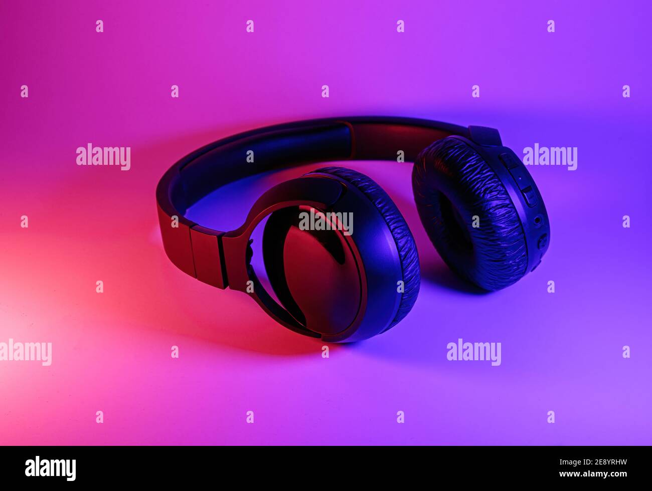 Eleganti cuffie wireless nere illuminate con coloratissima luce al neon su sfondo astratto isolato. Concetto di tecnologia moderna con spazio di copia Foto Stock