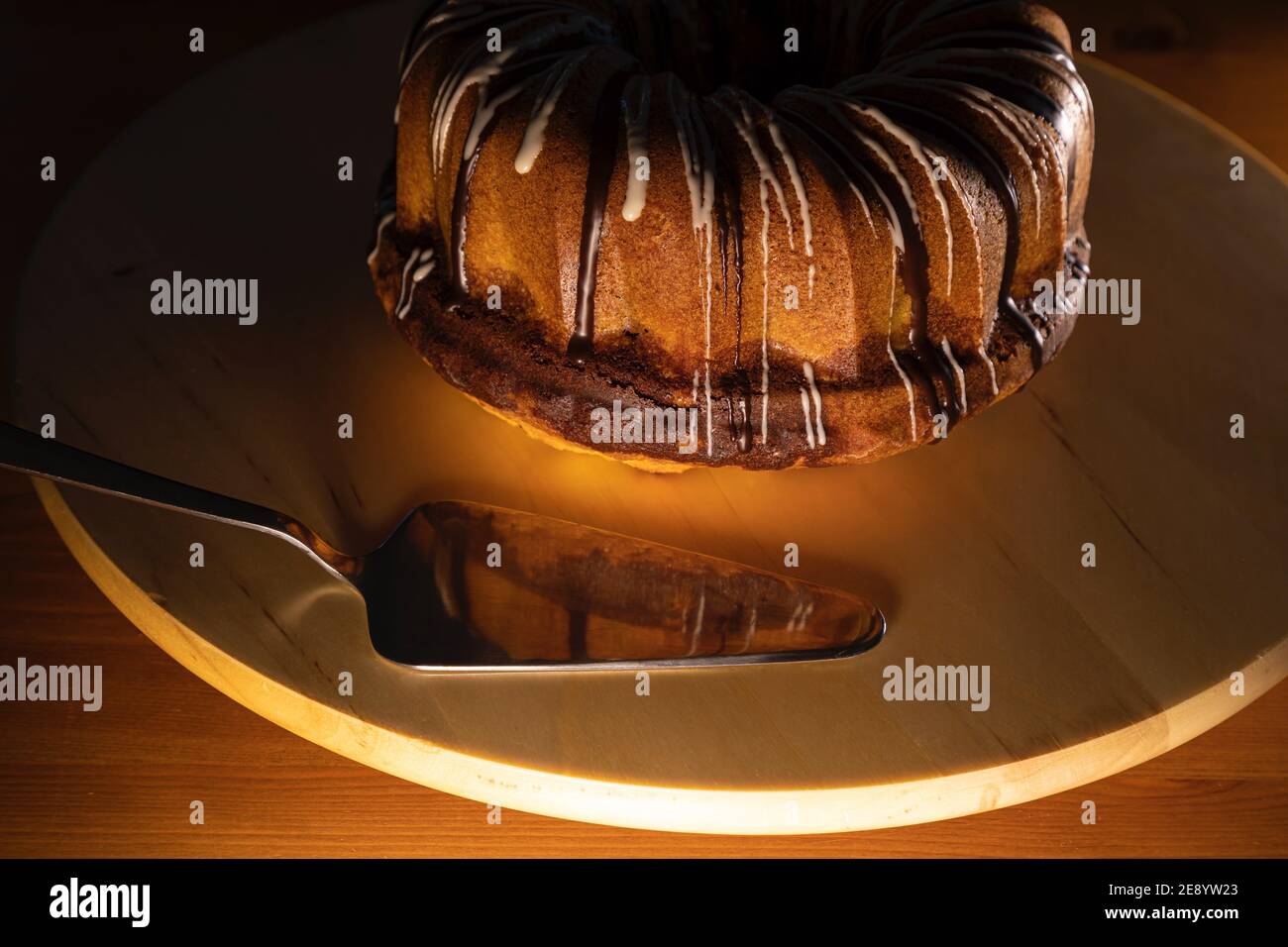 torta brundt ricoperta di zucchero di canna su un giradischi bianco con pala per torta d'argento, l'immagine è messa a fuoco sulla parte anteriore della torta e la pala, calda e bassa luce Foto Stock