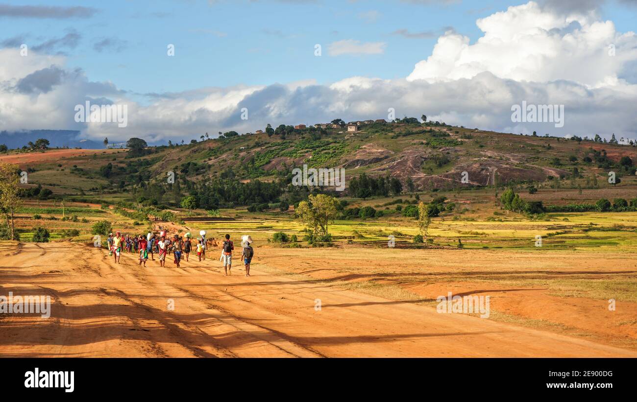 Sendrisoa, Madagascar - 28 aprile 2019: Gruppo di uomini, donne e bambini malgasci sconosciuti che camminano a casa dopo aver lavorato nei campi, sulla strada della polvere rossa, gr Foto Stock