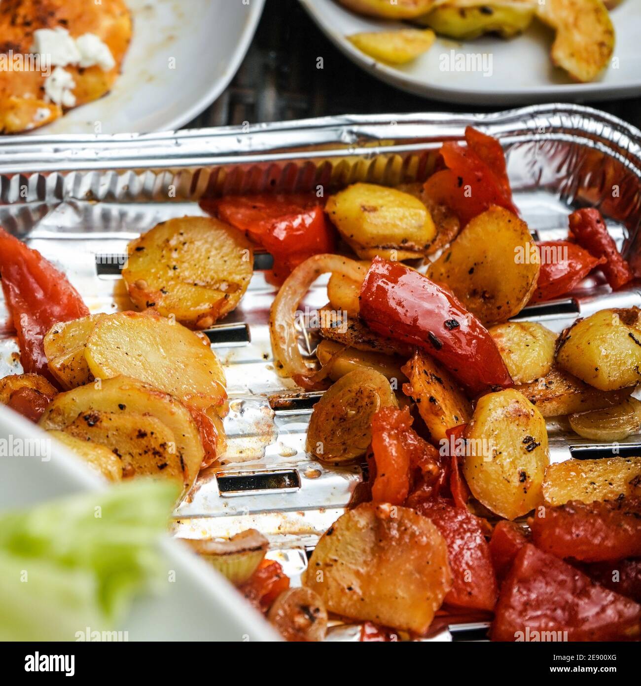 Patate alla griglia e pomodori serviti su vassoio in alluminio direttamente dalla griglia, dettaglio primo piano Foto Stock