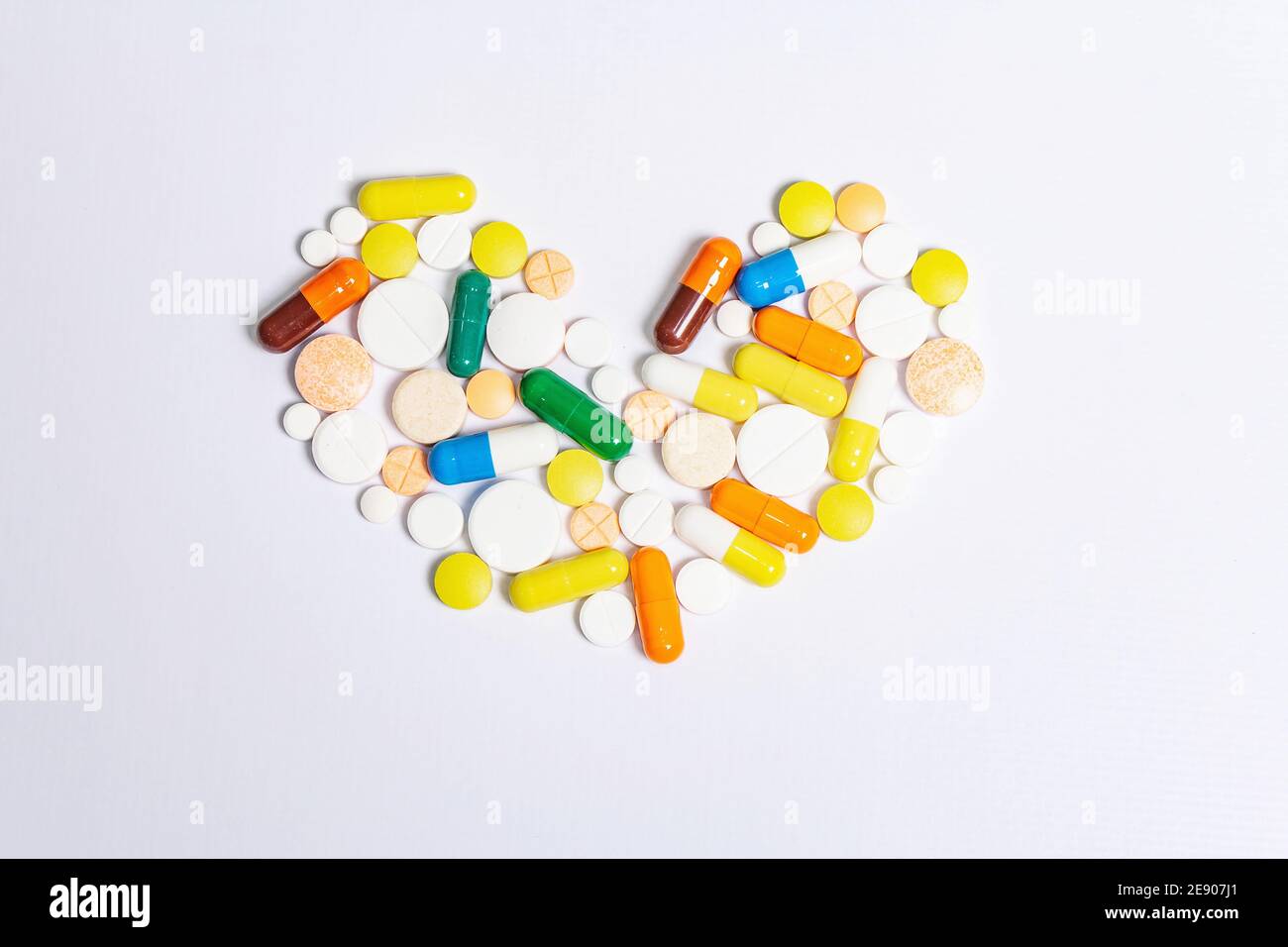 Pillole, compresse e capsule di medicina farmaceutica assortite per il trattamento delle malattie cardiache isolate su sfondo bianco. Forma del cuore, spazio di copia Foto Stock