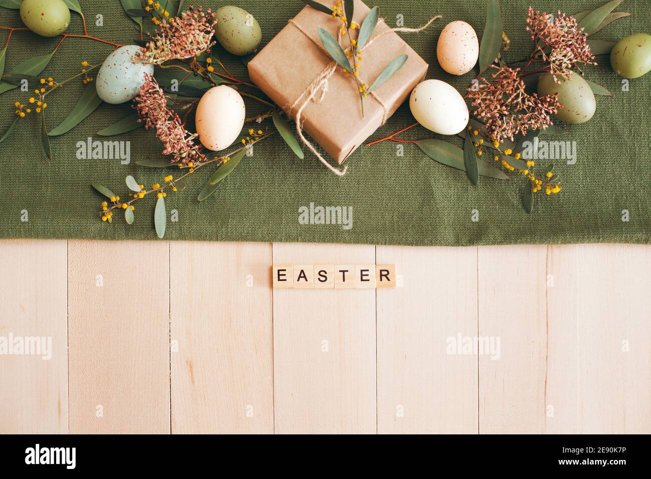 Tavolo di legno bianco con piatto e ciotola bianchi, uova di Pasqua color pastello, fiori freschi da giardino e carta marrone in confezione regalo, runner da tavolo verde Foto Stock