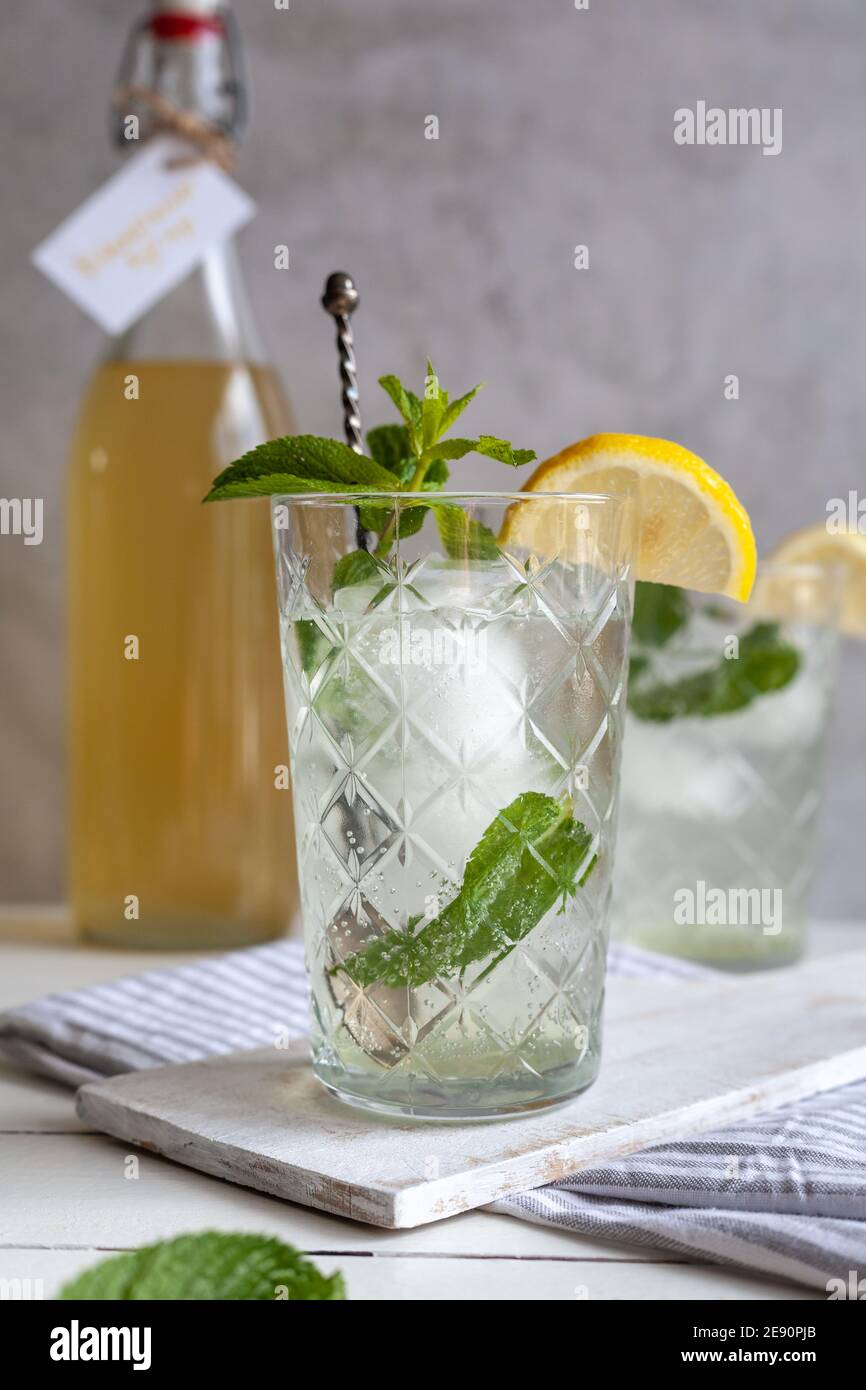 Bevanda rinfrescante alla limonata con ghiaccio, limone e menta con bottiglia di sciroppo sullo sfondo, superficie leggera Foto Stock