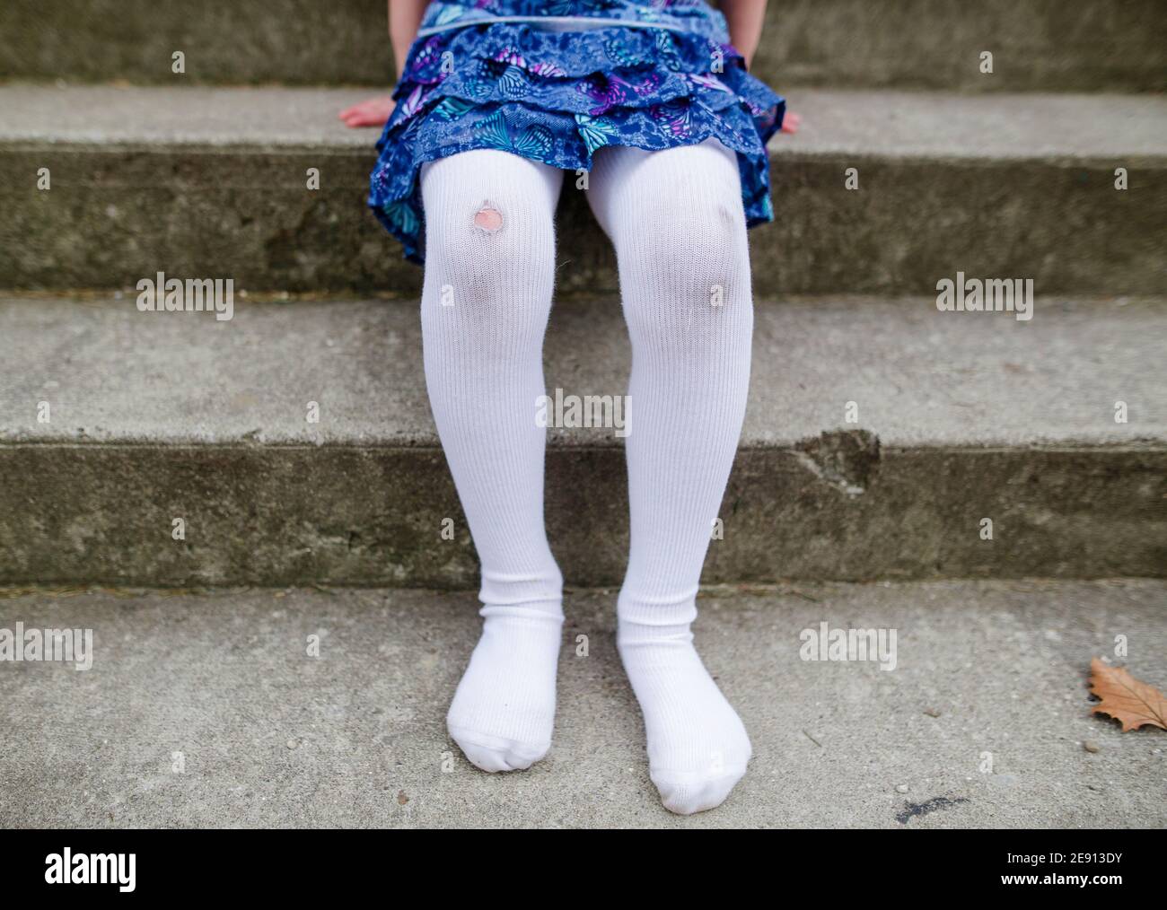 metà inferiore di bambina senza scarpe con collant strappati e. ginocchia sporche Foto Stock