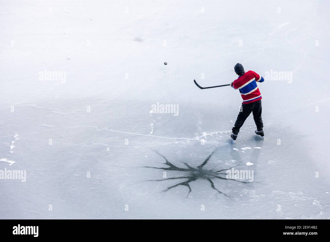 Da sopra anonimo uomo in uniforme tiro puck con bastone mentre si gioca a hockey vicino crack in ghiaccio di lago congelato in British Columbia, Canada Foto Stock