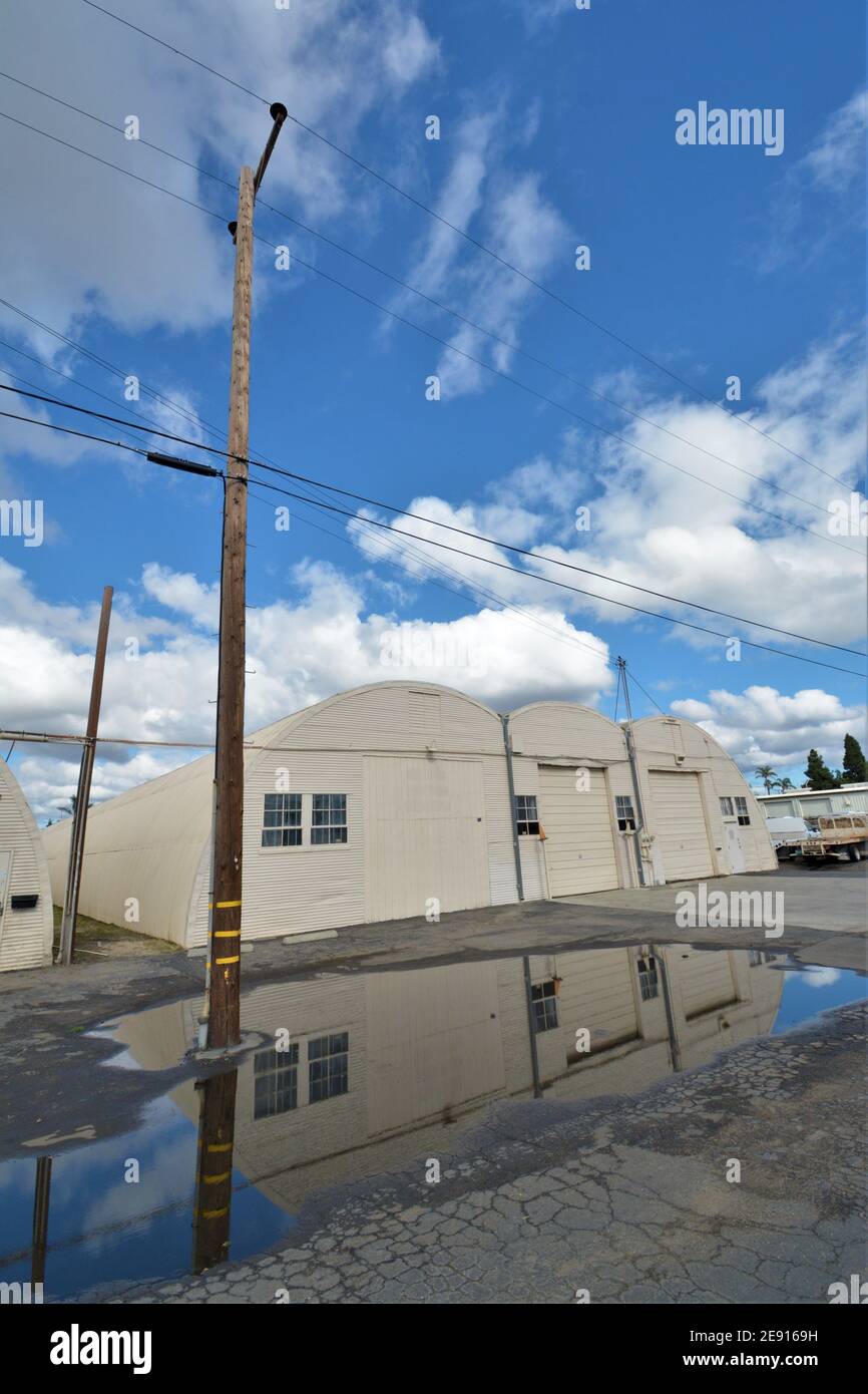 Guerra mondiale 2 medaglie Quonset capanna edifici dopo pioggia tempesta, con riflessione e cielo per spazio di copia, che sono ancora utilizzati per lo stoccaggio dopo 70 anni Foto Stock