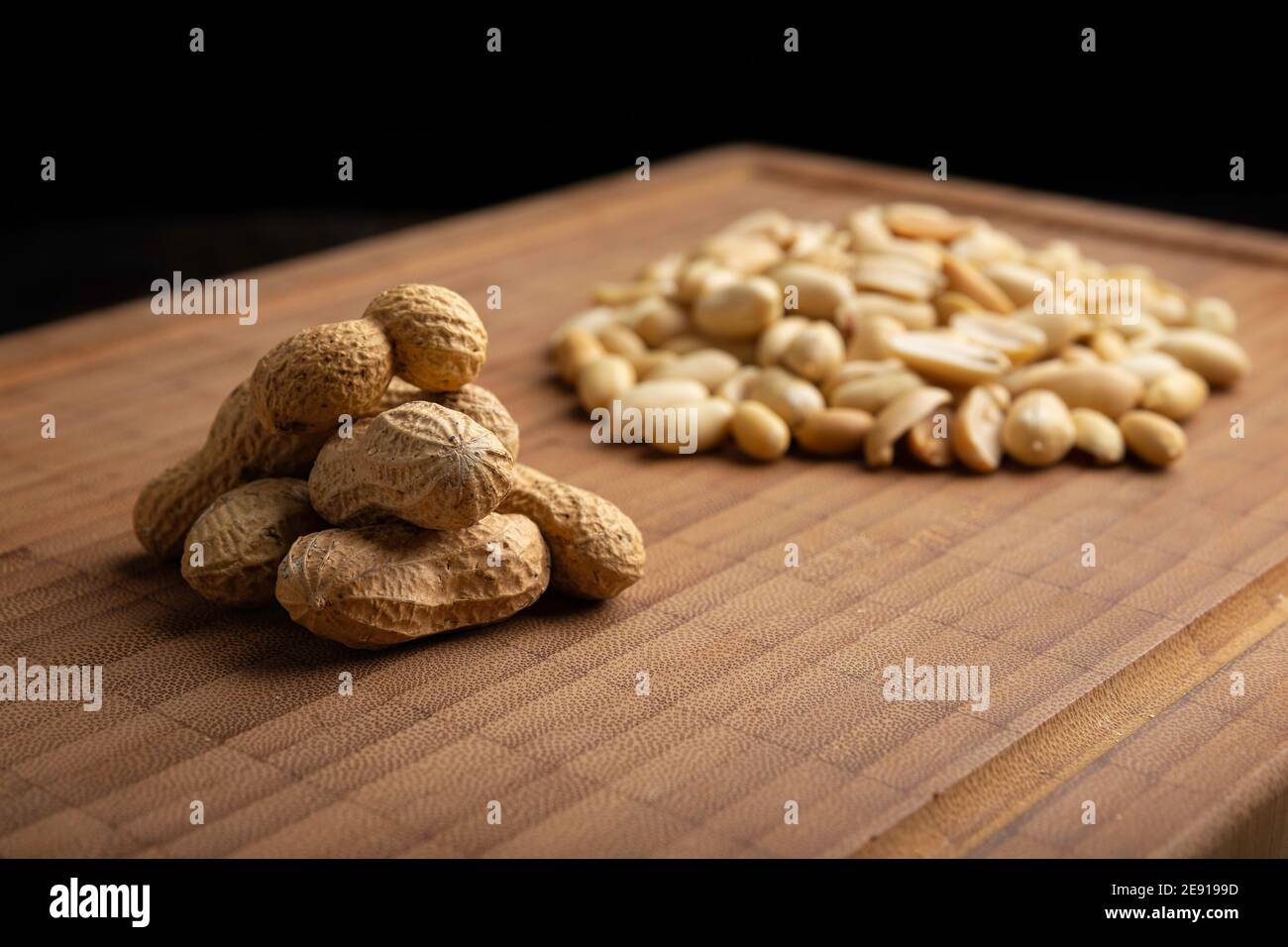 semi di arachidi sbucciate e non sbucciate e su tavola da taglio di bambù con fondo nero. (Arachis ipogaea) semi commestibili. Concetto di nutrizione sana dello snack Foto Stock