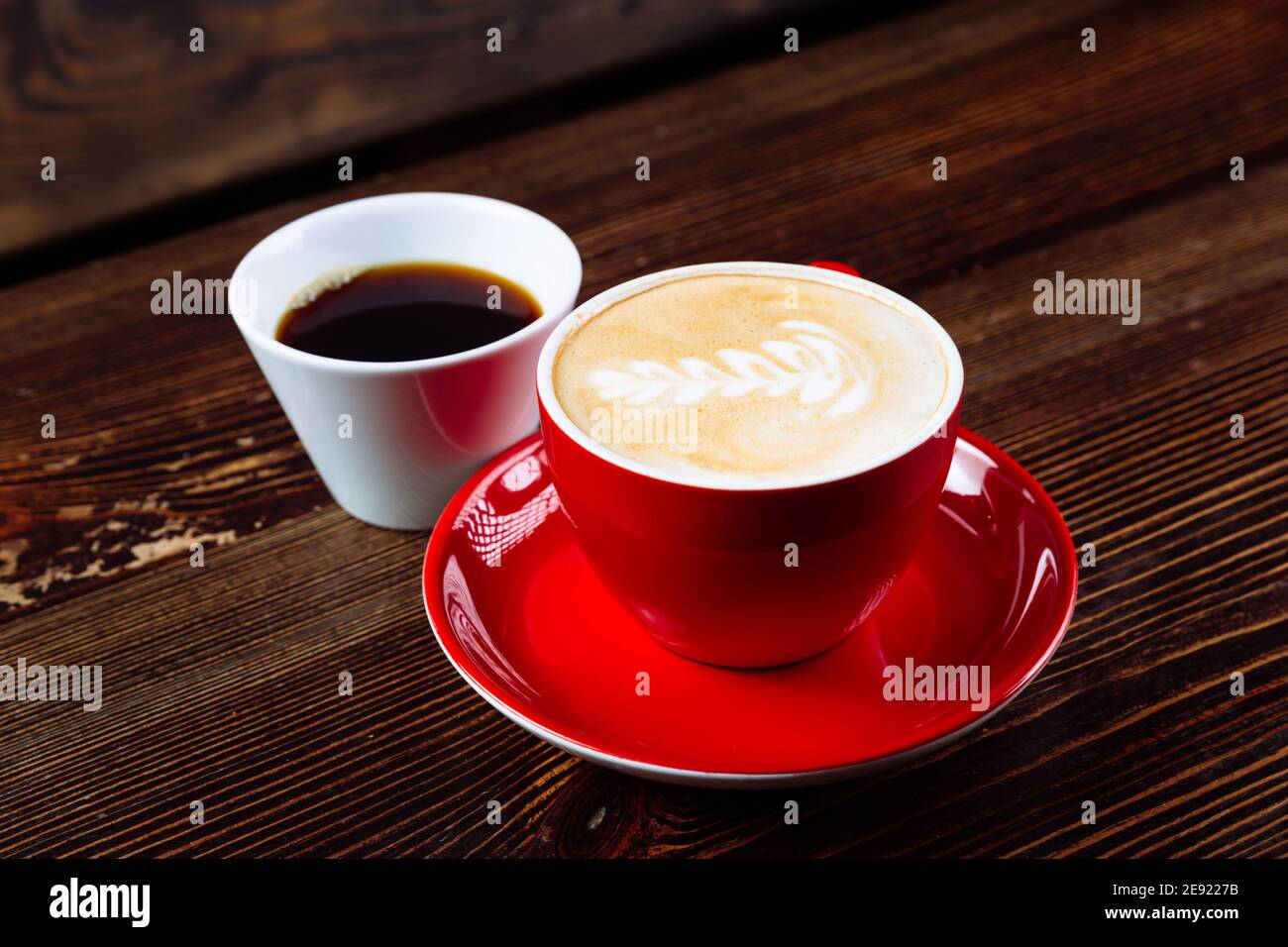 Caffè aromatico in una tazza rossa con schiuma di latte e latte art e caffè appena fatto in una tazza bianca su un tavolo di legno scuro. La scelta del caffè. Foto Stock