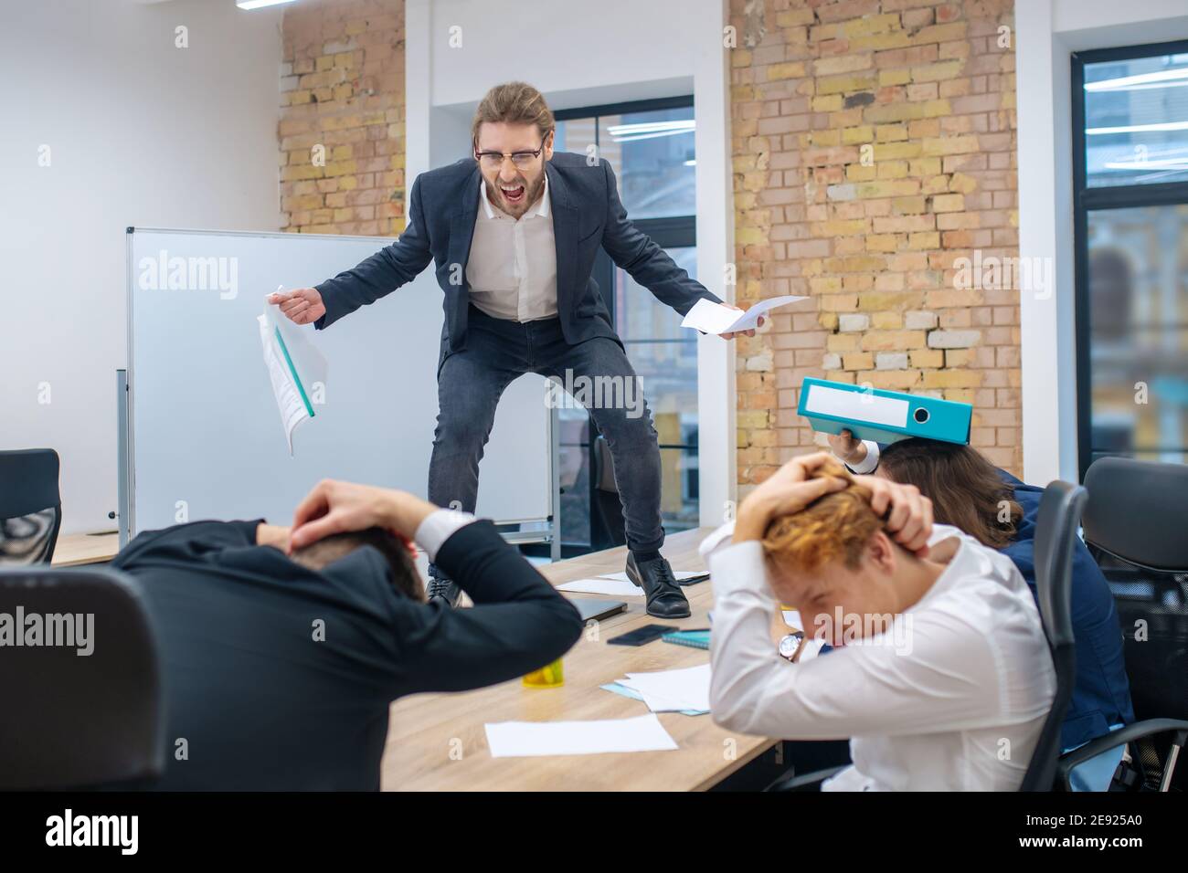 Uomo arrabbiato in piedi sul tavolo e dipendenti spaventati Foto Stock